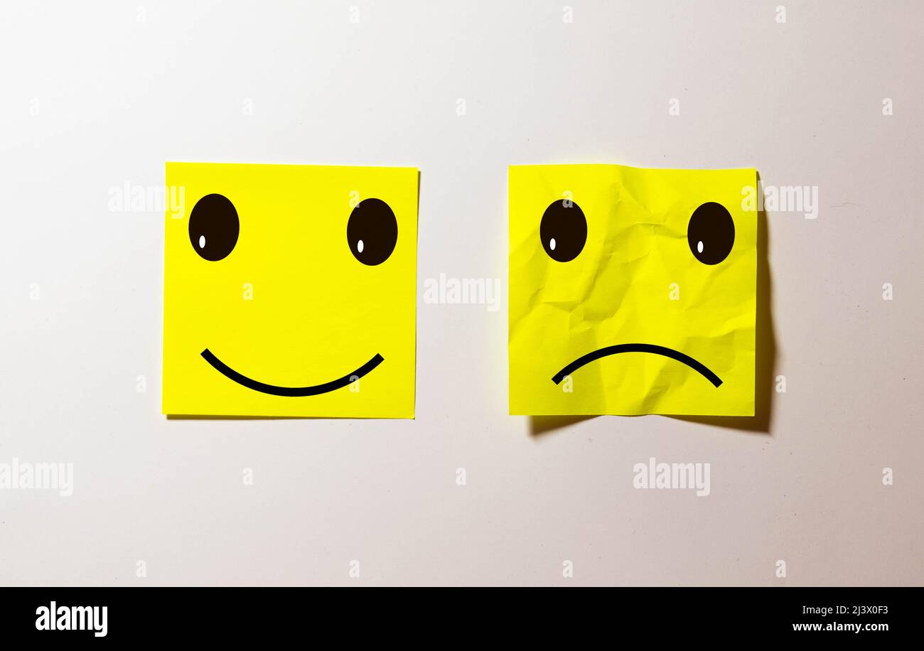 two notes stuck on message cork board with smiley and sad cartoon face expression in happiness versus depression and smile against adversity concept Stock Photo