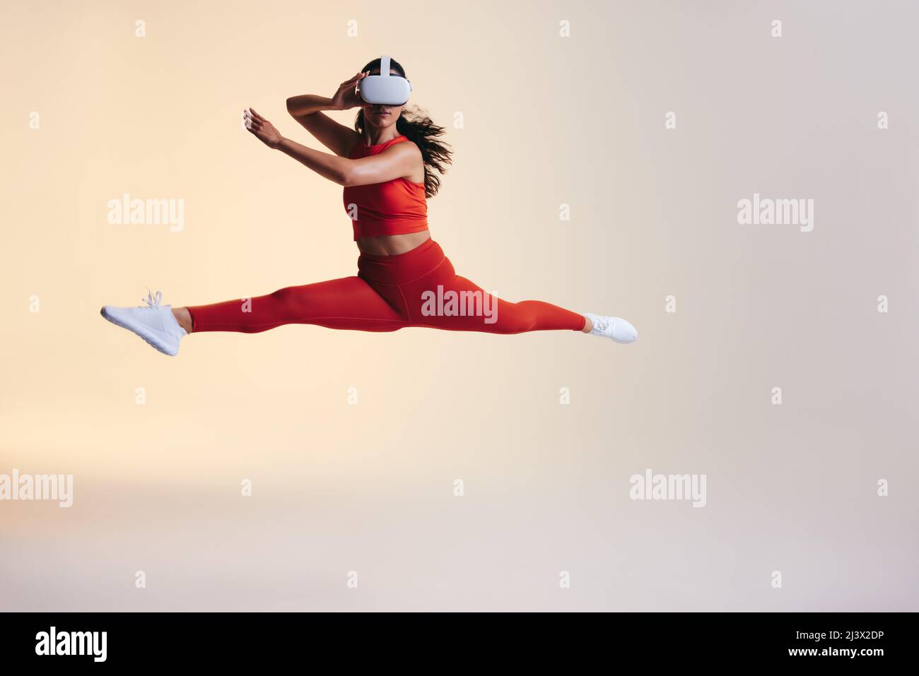 Fit young woman training with 3D technology. Athletic young woman jumping mid air while wearing a virtual reality headset. Active young woman explorin Stock Photo
