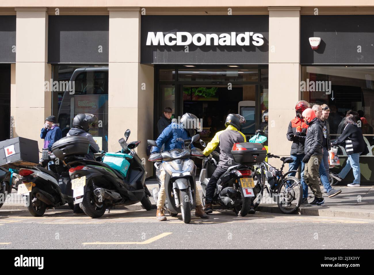 Gig economy. Motorcycle and cycle food delivery couriers gather outside a branch of McDonalds awaiting work in Newcastle upon Tyne, UK. Stock Photo