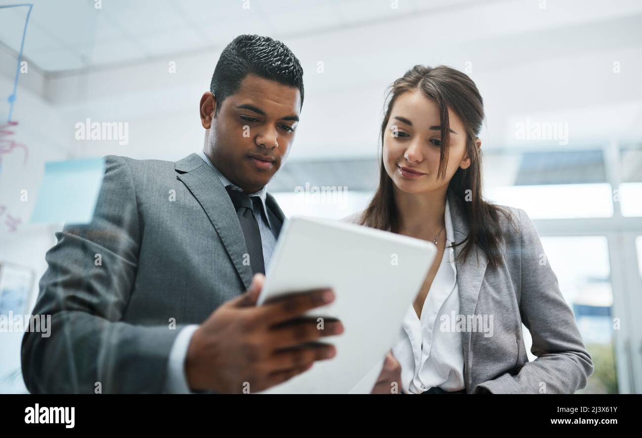 Keeping the numbers up with portable tech. Shot of a young businessman and businesswoman using a digital tablet in a modern office. Stock Photo