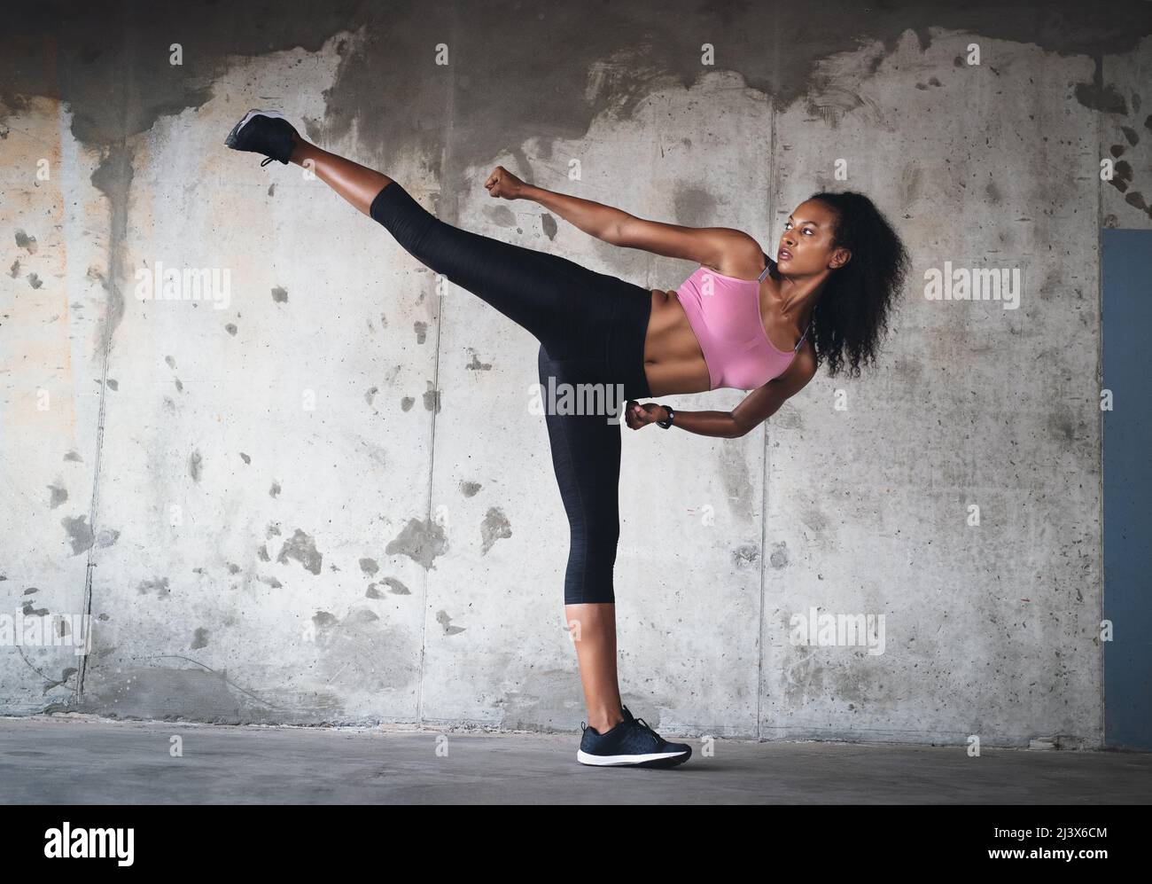 Balance is everything. Full length shot of a young sportswoman kicking up her leg in the air while exercising inside a parking lot. Stock Photo