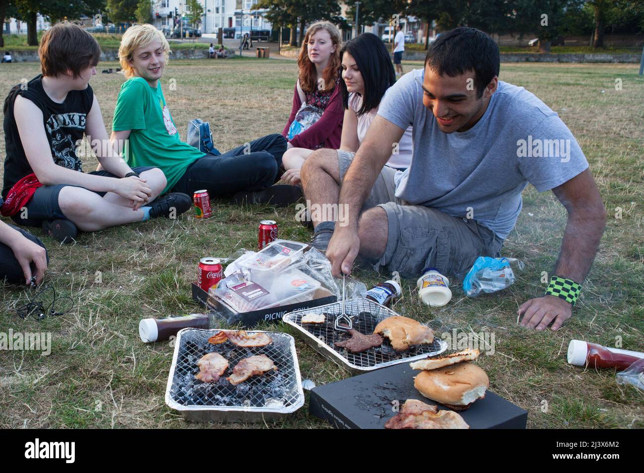 A man cooking food on a disposable barbeque in a park in Brighton Stock Photo