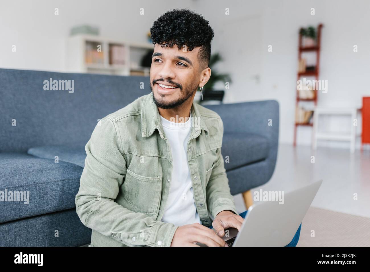 Casual young latino american man working on laptop sitting on floor at home Stock Photo