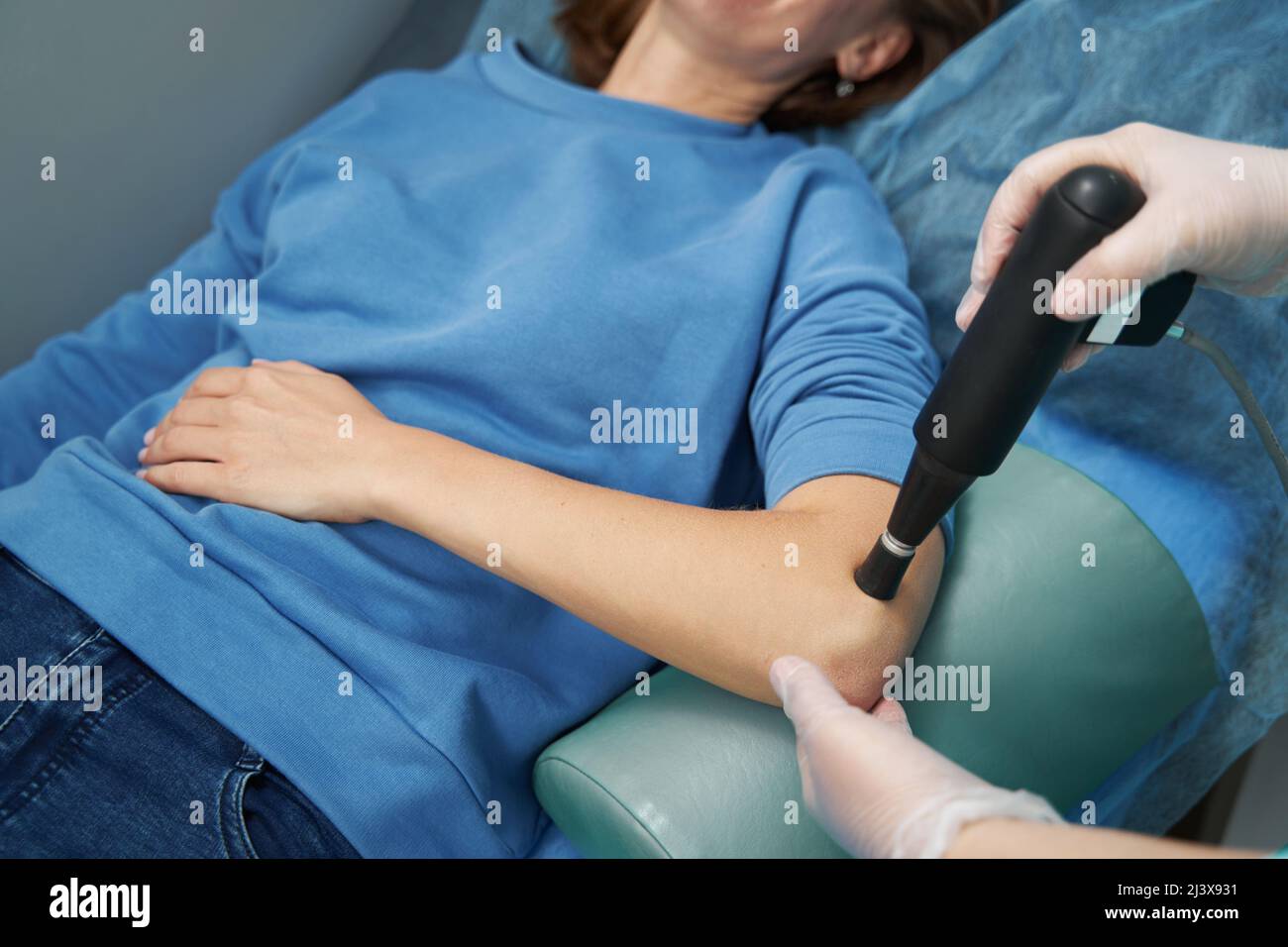 Doctor hands using pain relief device while performing physiotherapy procedure on woman elbow Stock Photo