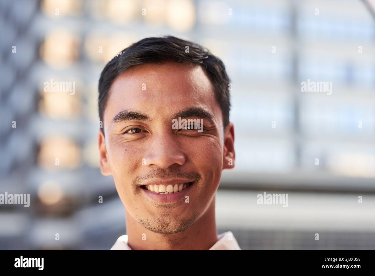 An attractive South East Asian man smiles for a portrait outside city building Stock Photo