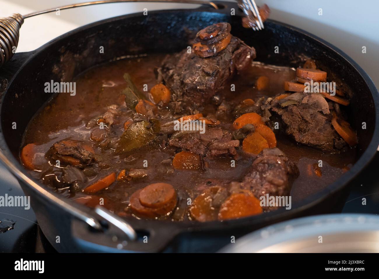 Braised beef cheeks cooking in red wine sauce in cast iron Dutch oven. Slow cooked meat stew. Stock Photo