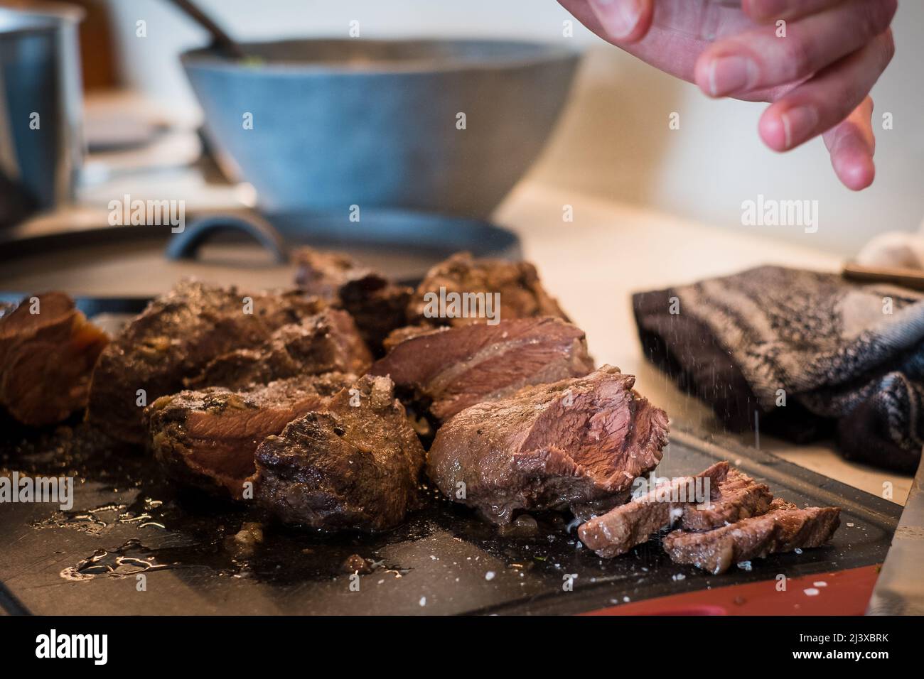 Salt falling on braised beef cheeks cooked in red wine sauce on cutting board. Slow cooked meat stew. Stock Photo