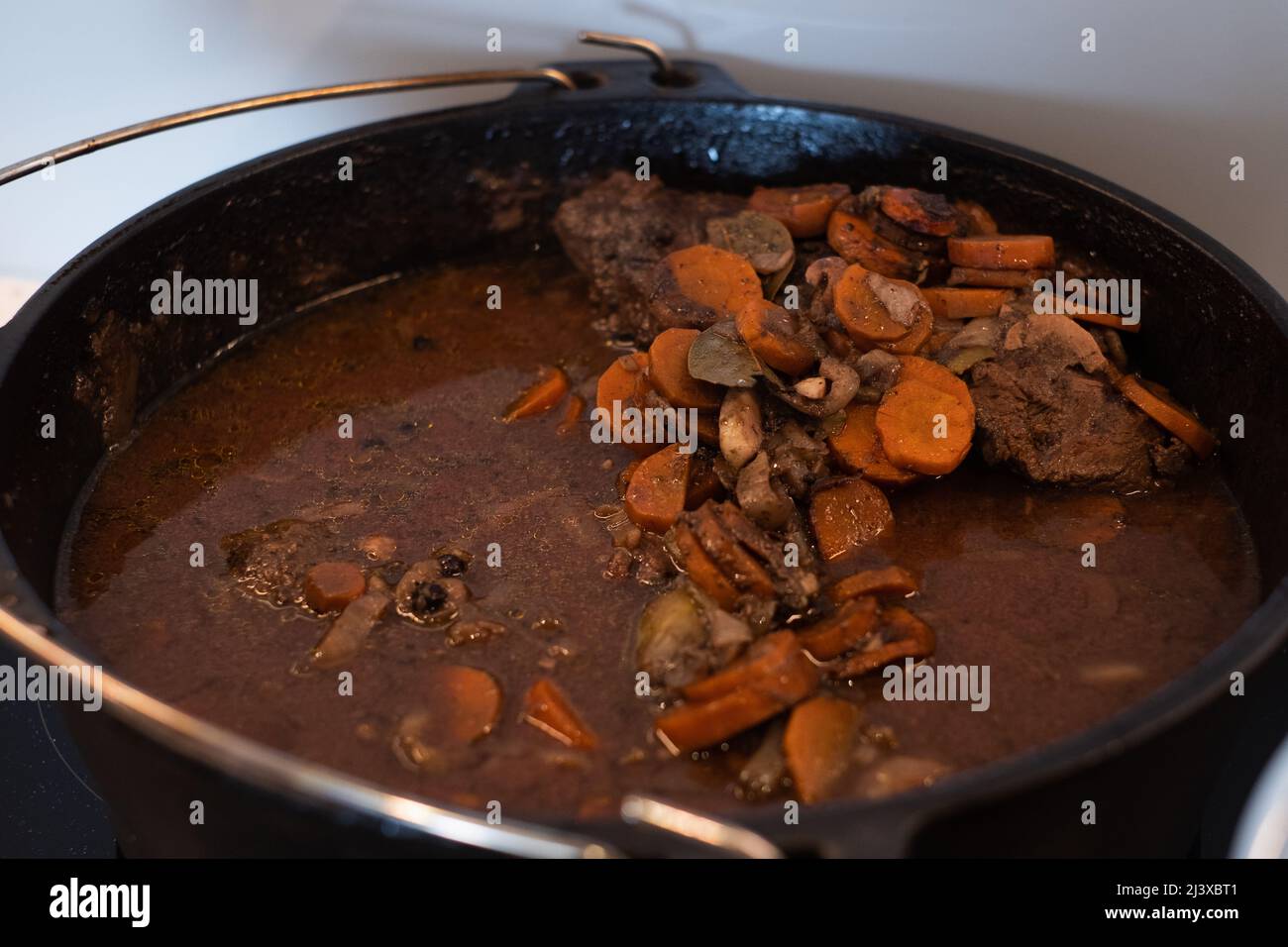 Braised beef cheeks cooking in red wine sauce in cast iron Dutch oven. Slow cooked meat stew. Stock Photo