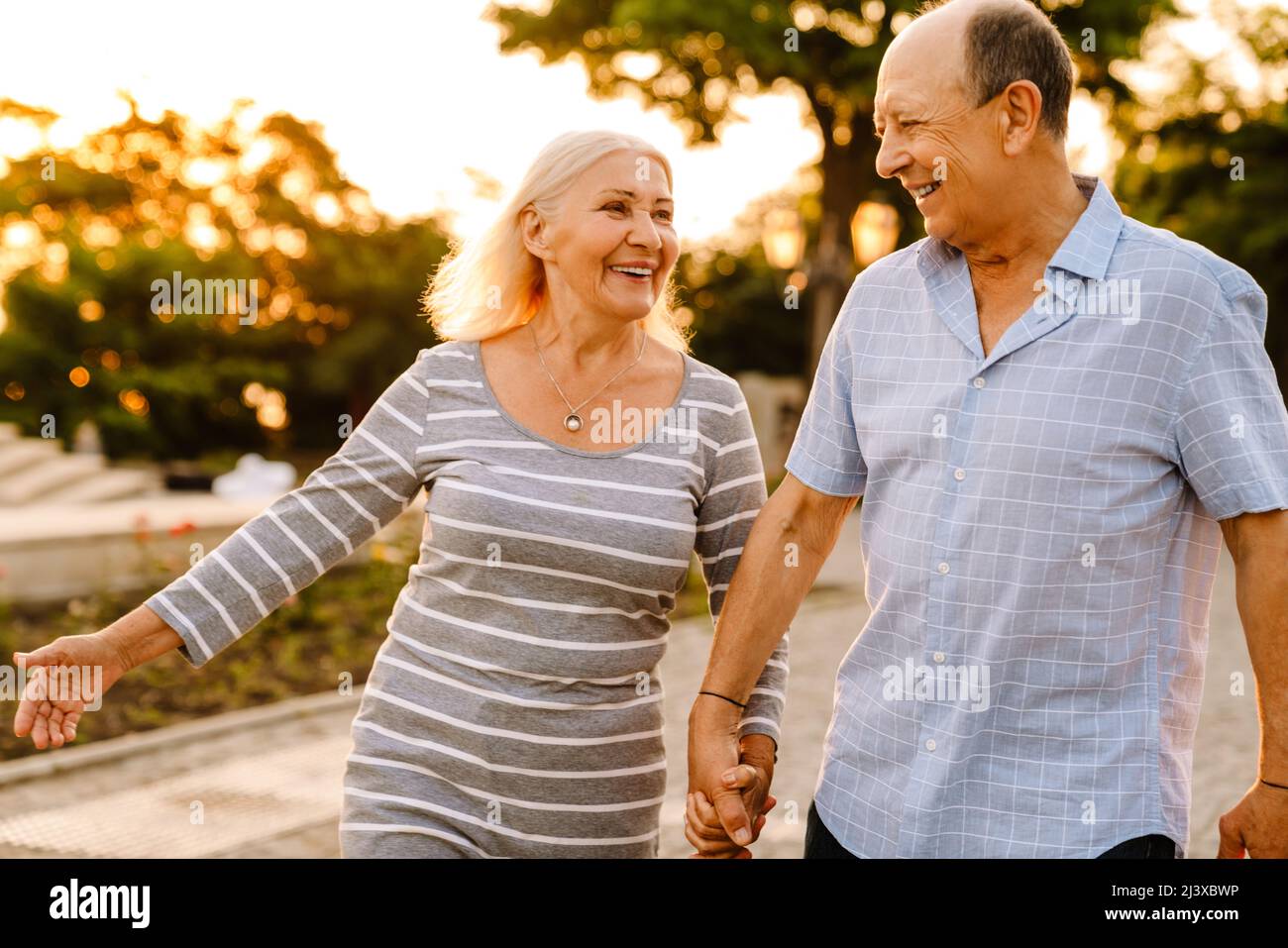 White senior couple holding hands and smiling while walking in summer ...