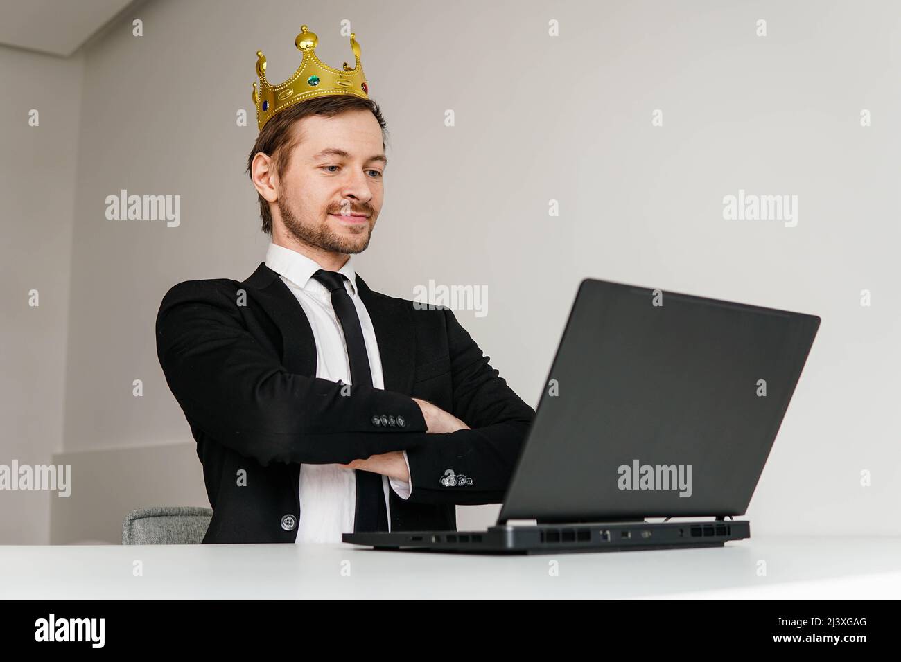 Self-confident arrogant businessman with golden crown on head using laptop. Stock Photo