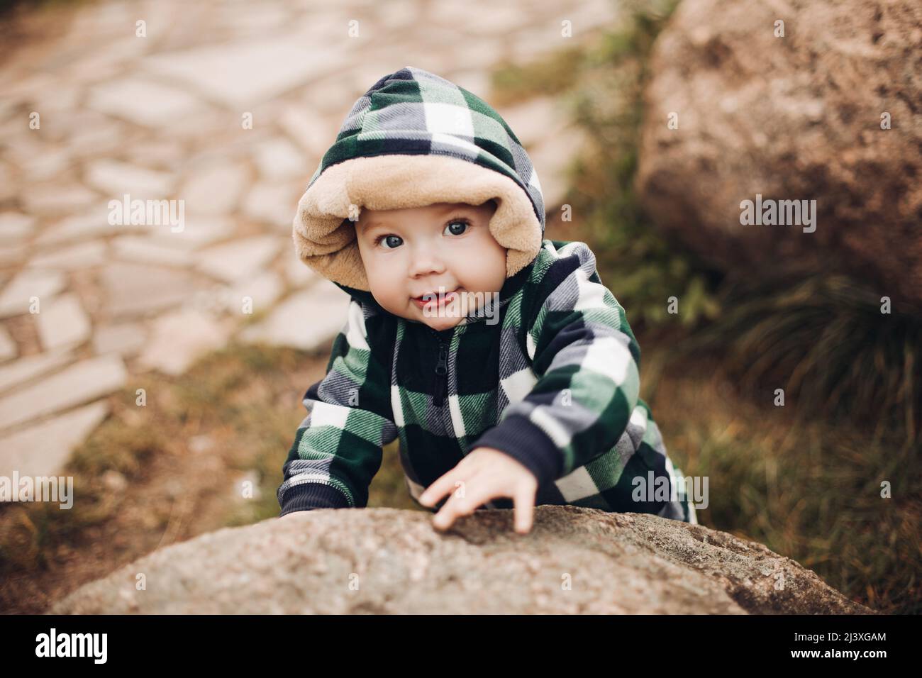 Adorable baby in warm overall with hood sitting on foliage Stock Photo -  Alamy