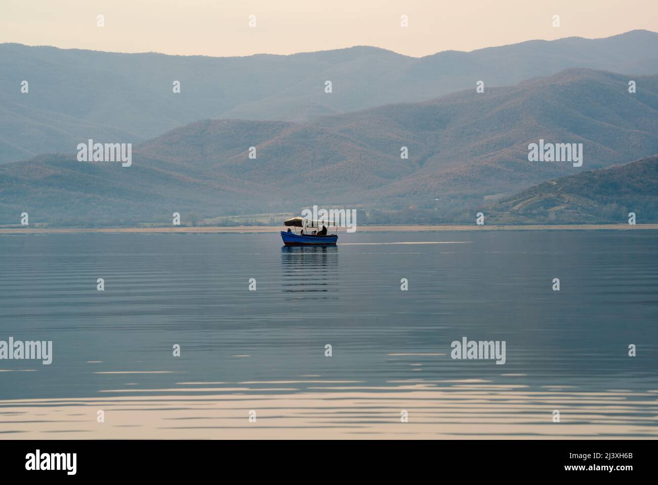 Scenery of boat with people floating in the lake on a beautiful morning light. Picturesque art background of a boat in a lake. Stock Photo