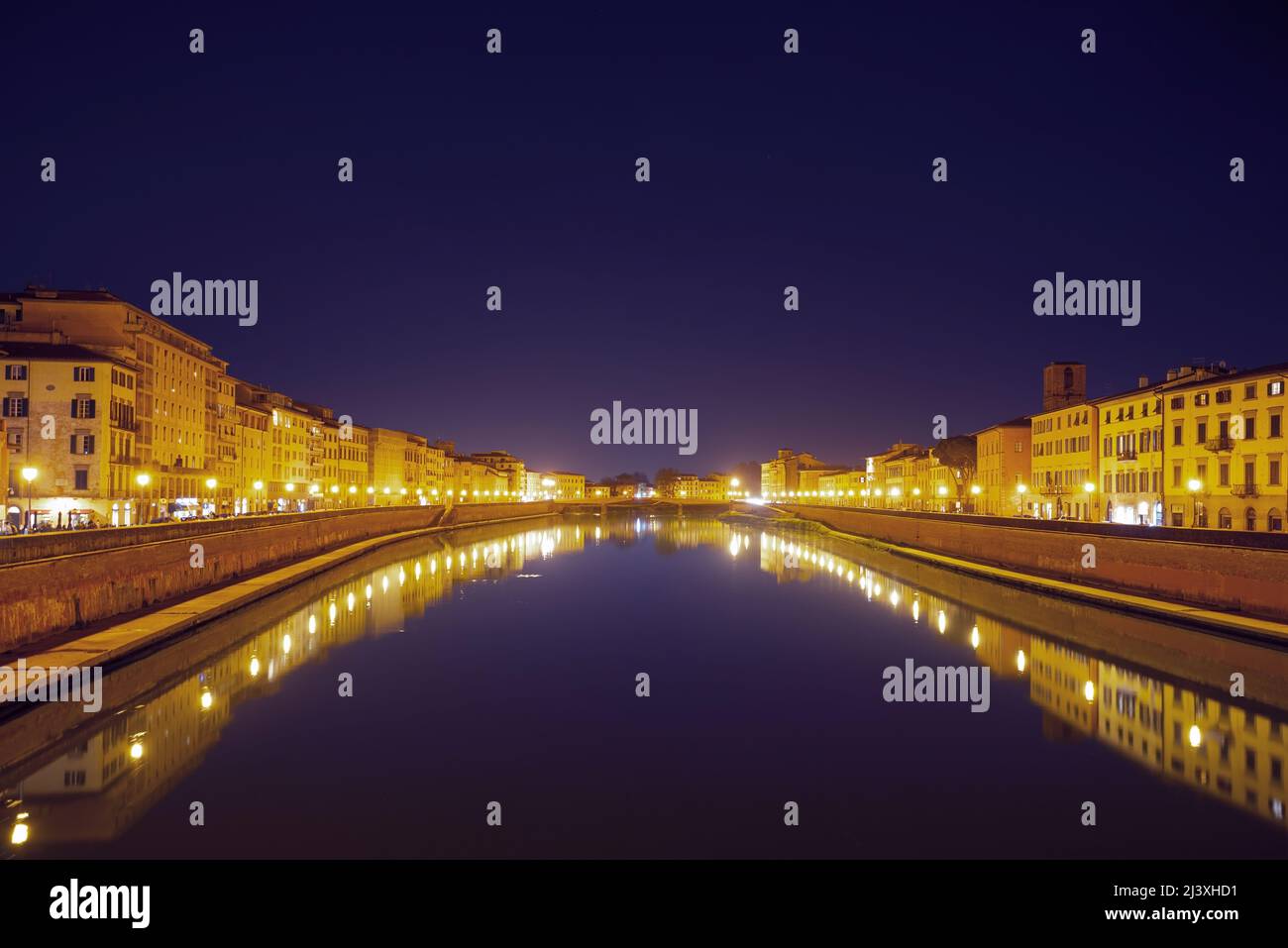 Houses lit with golden light and their reflections in the Arno River at night in Pisa, Italy. Panoramic view Stock Photo
