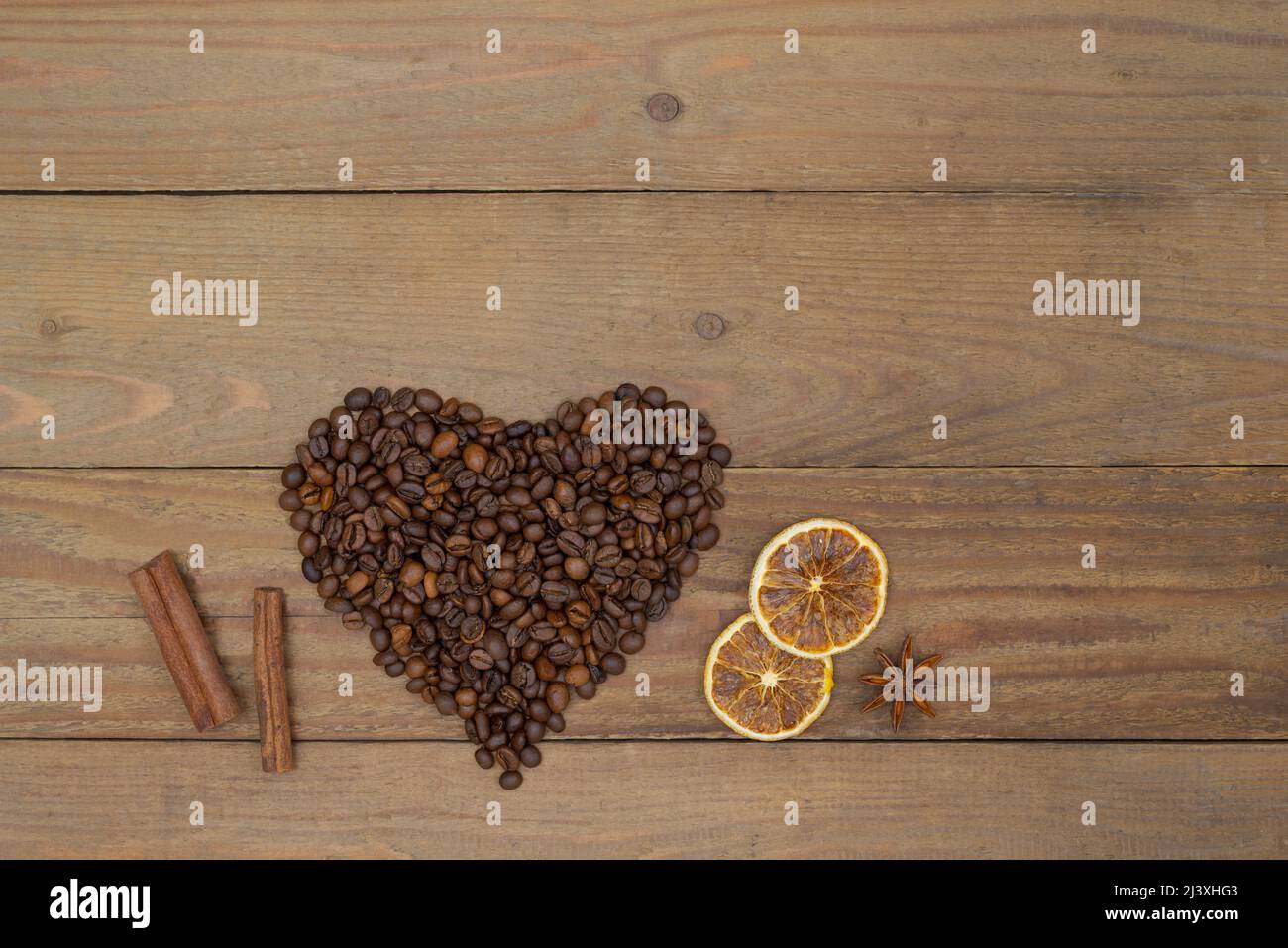 Coffee beans heart shape, cinnamon sticks and dry lemon slices on an old wooden background. Coffee design concept. Stock Photo