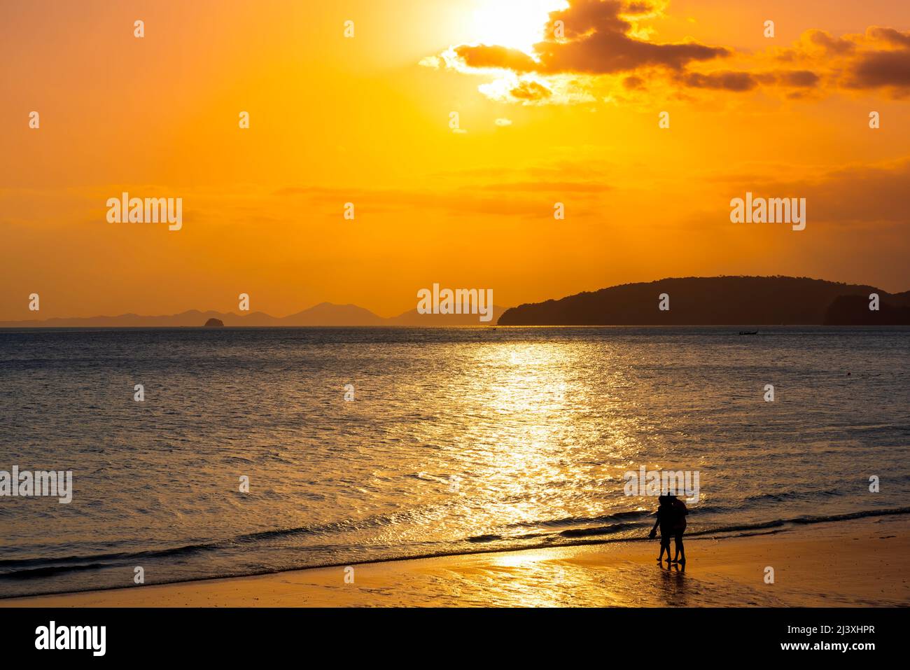 Relaxing sea sunset and romantic couple silhouettes walking on the beach in golden sunlight. Stock Photo