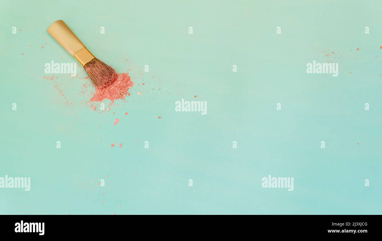 Top view of a small blush applicator brush, with a pile of pinkish makeup powder center around the brush head. On a bluish green background. Stock Photo