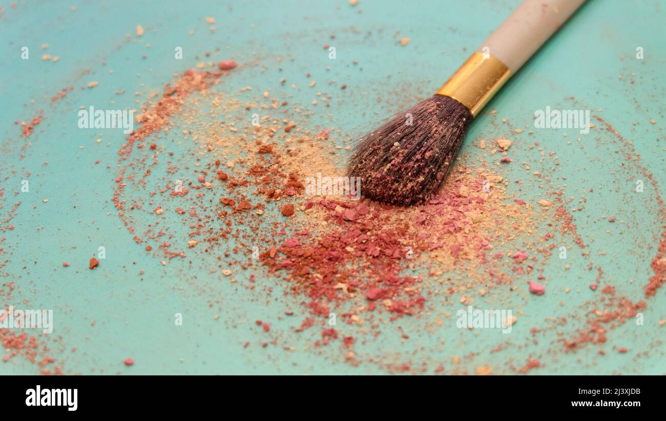 A large blush applicator brush, with a pile of red and cream color makeup powder center around the brush head. On a bluish green background. Stock Photo