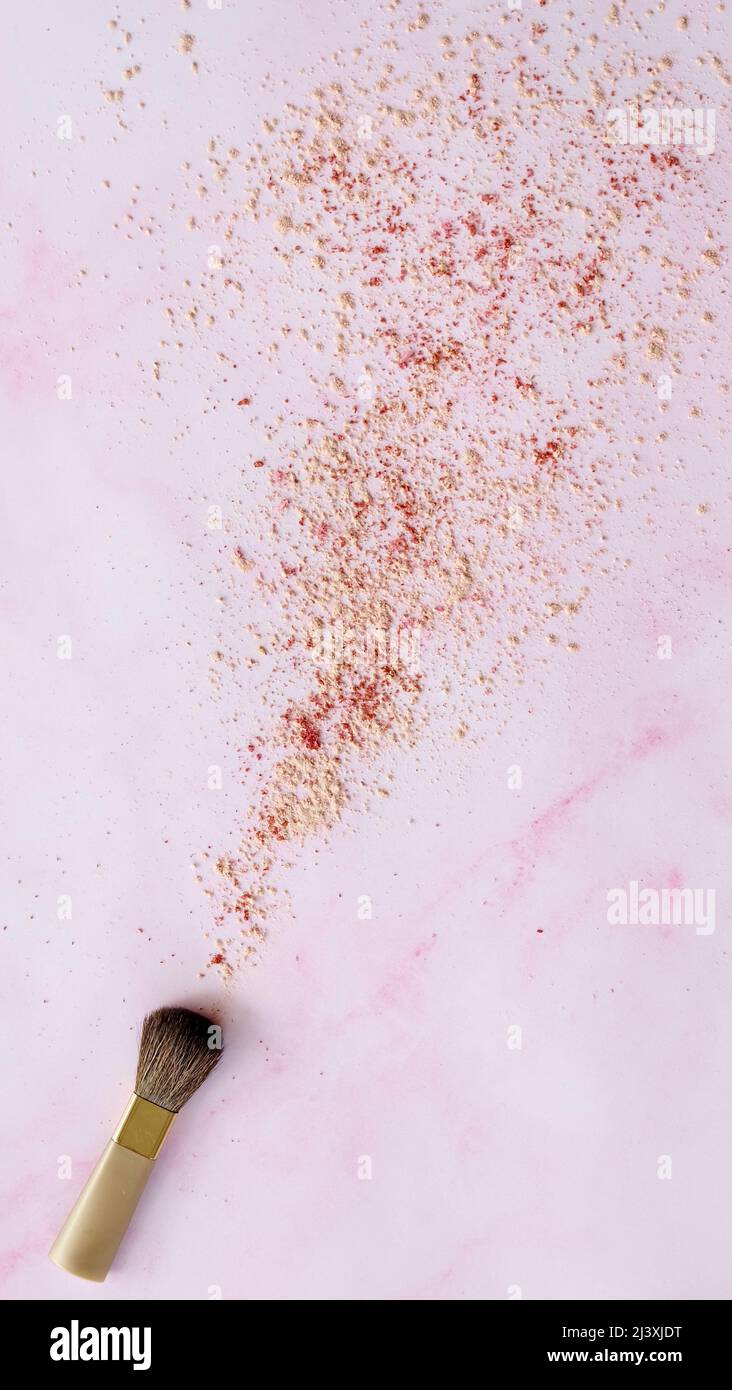 Top view of a makeup brush, with cosmetic powder spreading out from its tip. On a pink marble like surface. Stock Photo