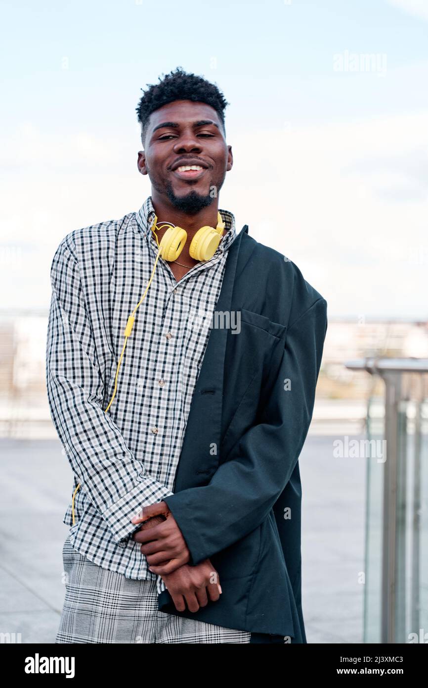 African-American man wearing a mid-length blazer, yellow headphones and plaid shirt. Stock Photo