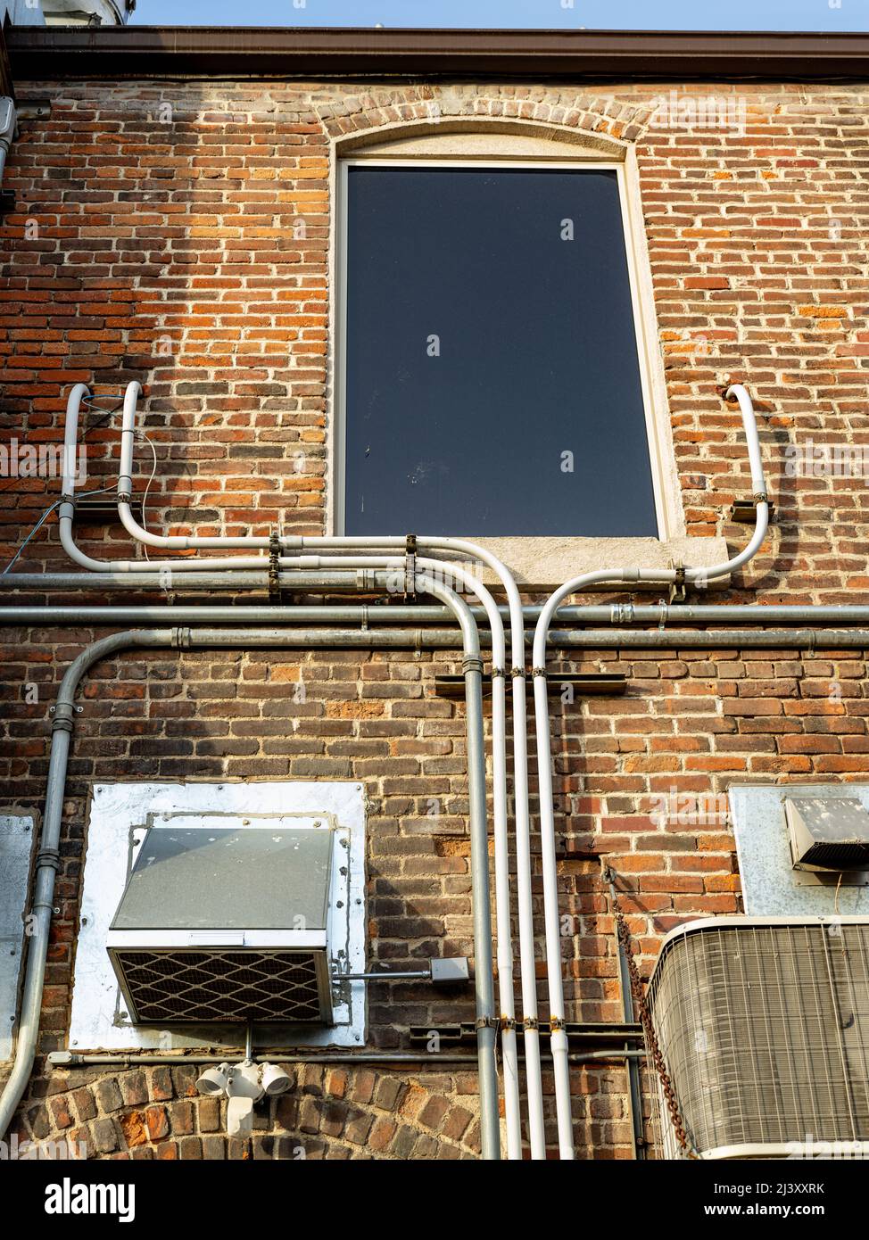 Abstract brick building wall with exterior plumbing and window Stock