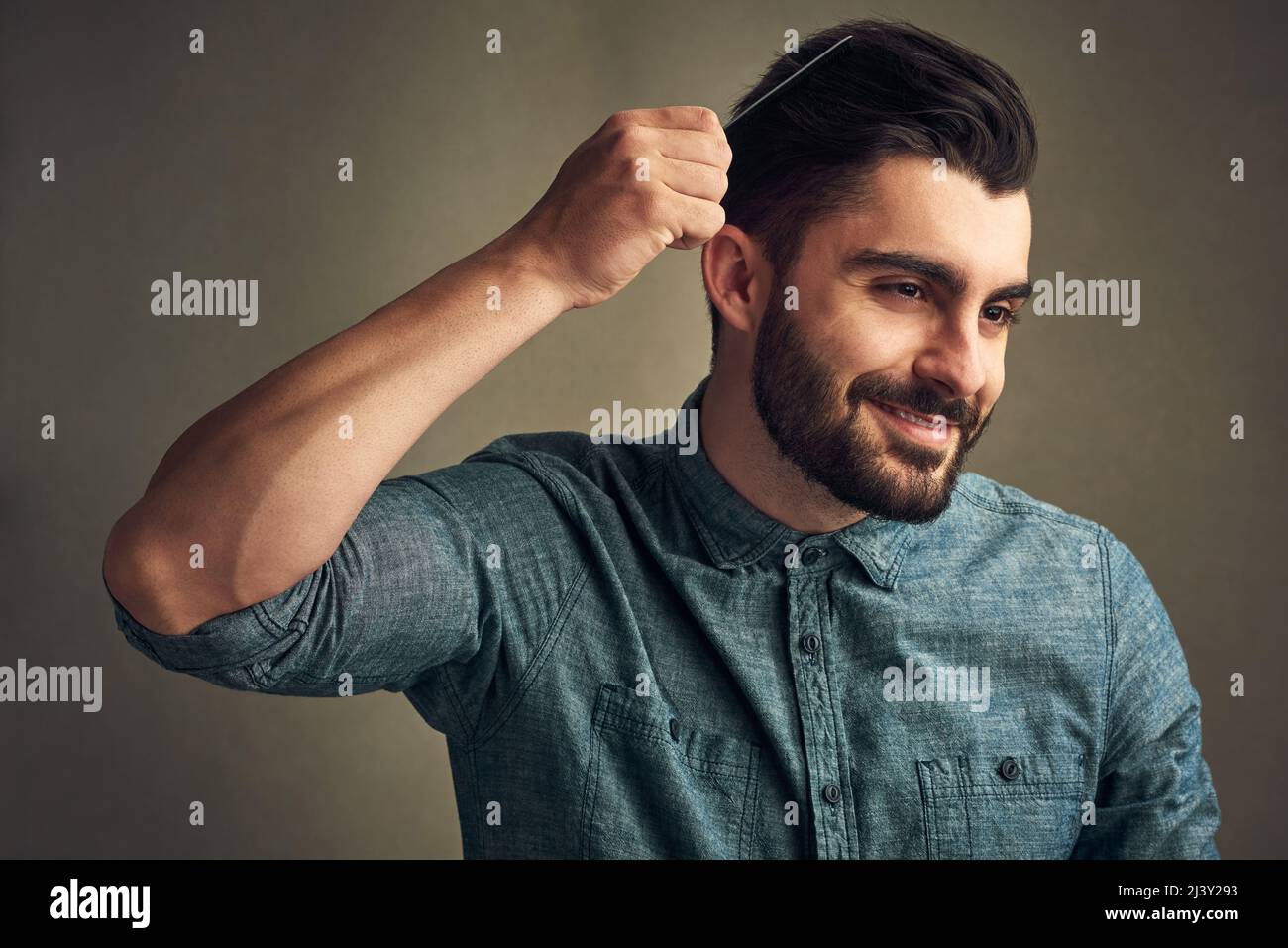 Have you ever seen anything so beautiful. Studio shot of a handsome young man combing his hair against a grey background. Stock Photo