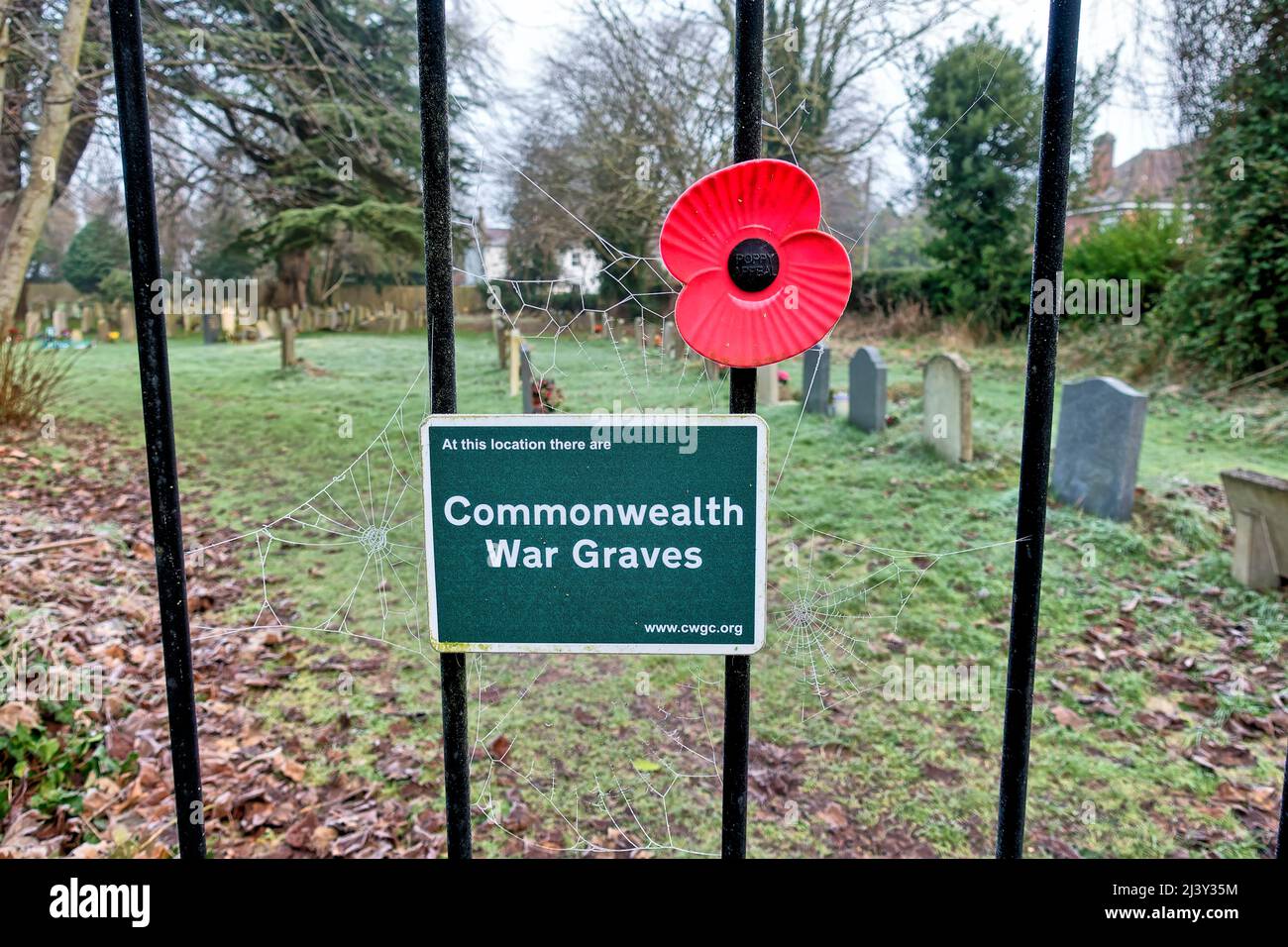 Warminster, Wiltshire,UK - January 18 2022: A Commonwealth War Graves sign and a Red Plastic Remembrance poppy on a churchyard gate at St Johns church Stock Photo