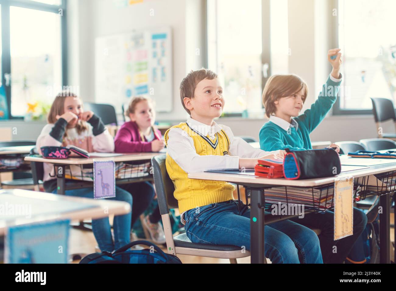 Pupils in elementary school class raising hands to answer Stock Photo