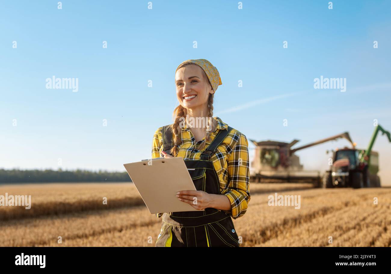 Farmer on grain field with tractor and combine harvester in background Stock Photo