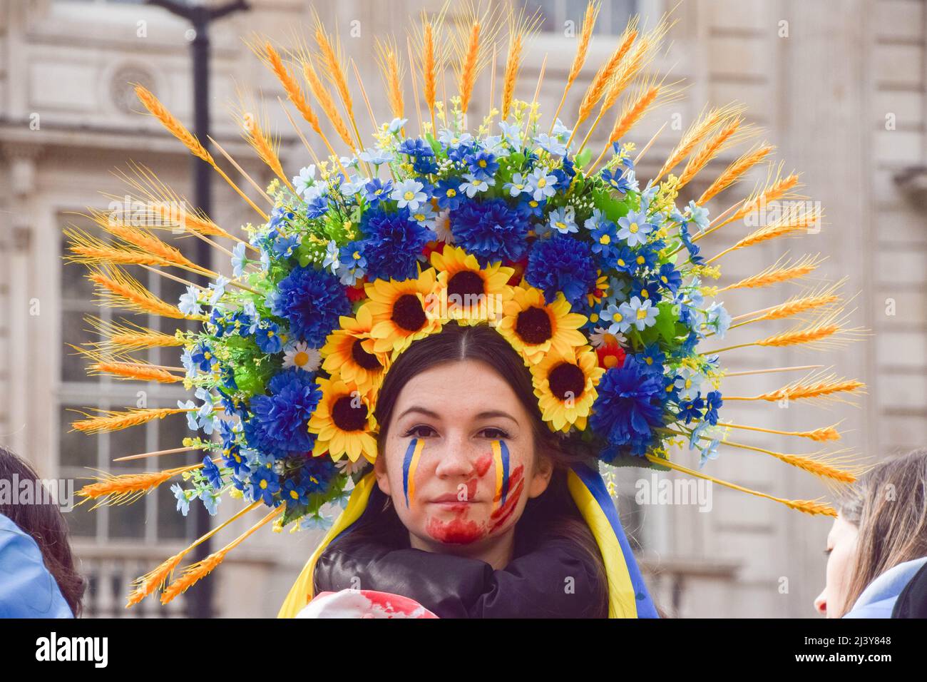 London, UK. 10th Apr, 2022. A protester wearing an ornate flower headdress, a palm print with fake blood and colours of the Ukrainian flag painted on her face is seen during the demonstration outside Downing Street. Demonstrators gathered in solidarity with Ukraine, as reports emerge of massacres in Bucha and other towns and cities in Ukraine and atrocities reportedly committed by Russian troops. Credit: SOPA Images Limited/Alamy Live News Stock Photo