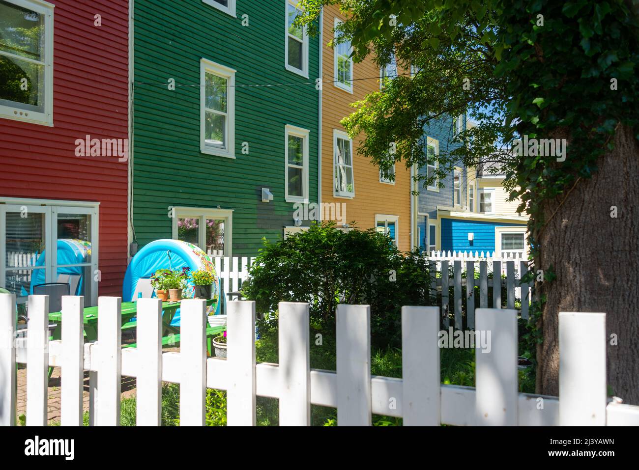 An upward view of an exterior of multiple joined colorful wooden houses with double hung windows. There are red, green, yellow, and blue houses. Stock Photo