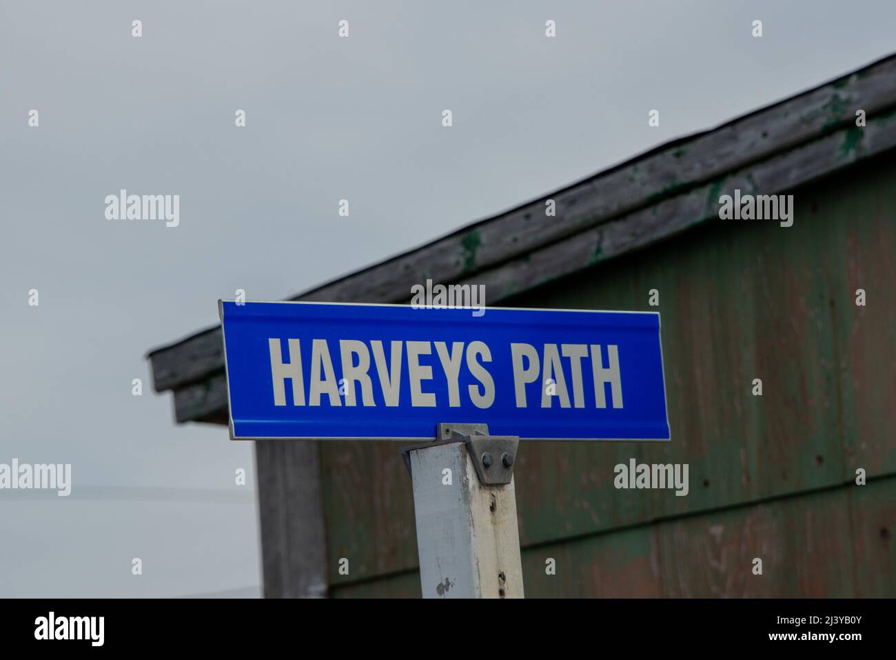 A blue metal street name sign is attached to a white square wooden post. The white text on the sign spells Harvey's Path in capital letters. Stock Photo