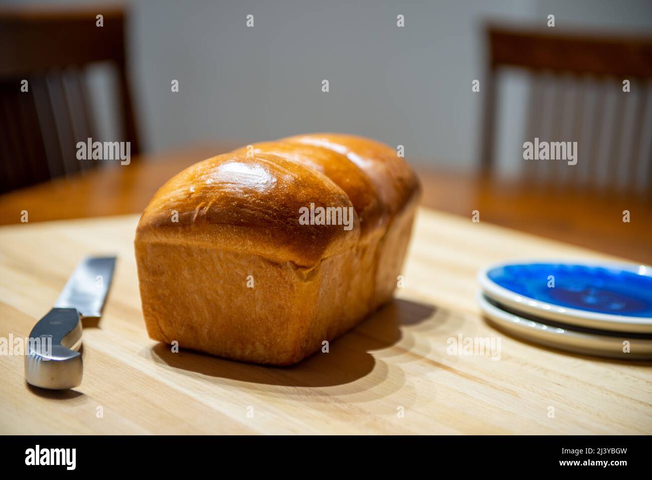 A single loaf of fresh white bread on a wooden cutting board in a kitchen. The warm crisp bun has melted butter over the crisp loaf. Stock Photo