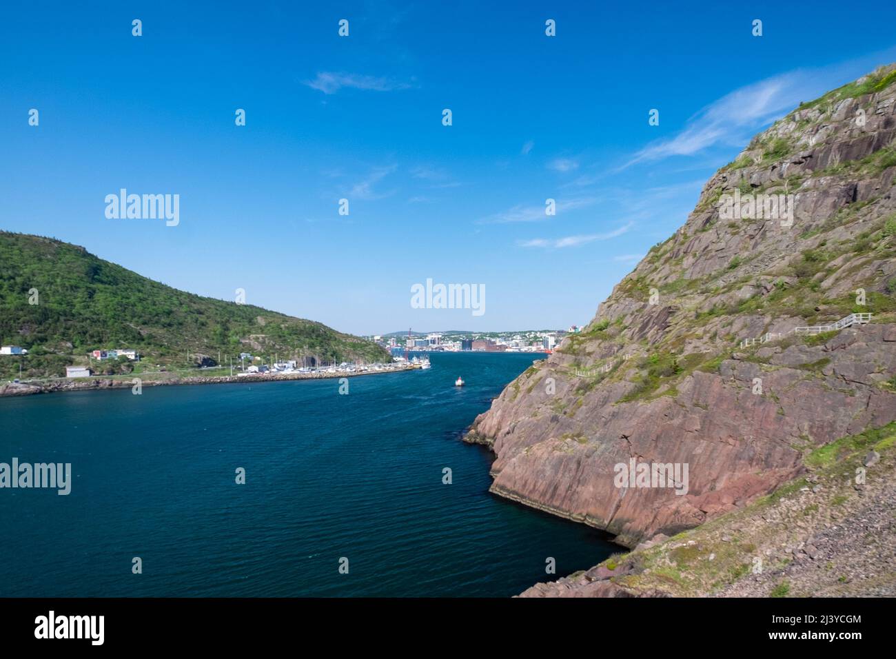 A footpath, Signal Hill hiking trail, or path in St. John's along a hillside. The cliff is rocky with grass patches. The ocean is blue in the harbor. Stock Photo