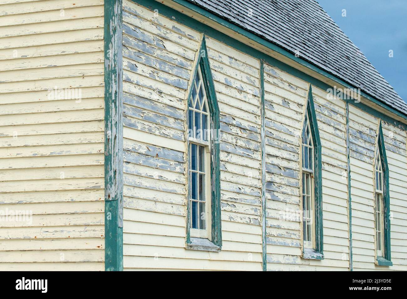 The exterior wall of a religious building with pale yellow colored narrow horizontal clapboard siding and tall Gothic-style windows with clear glass, Stock Photo