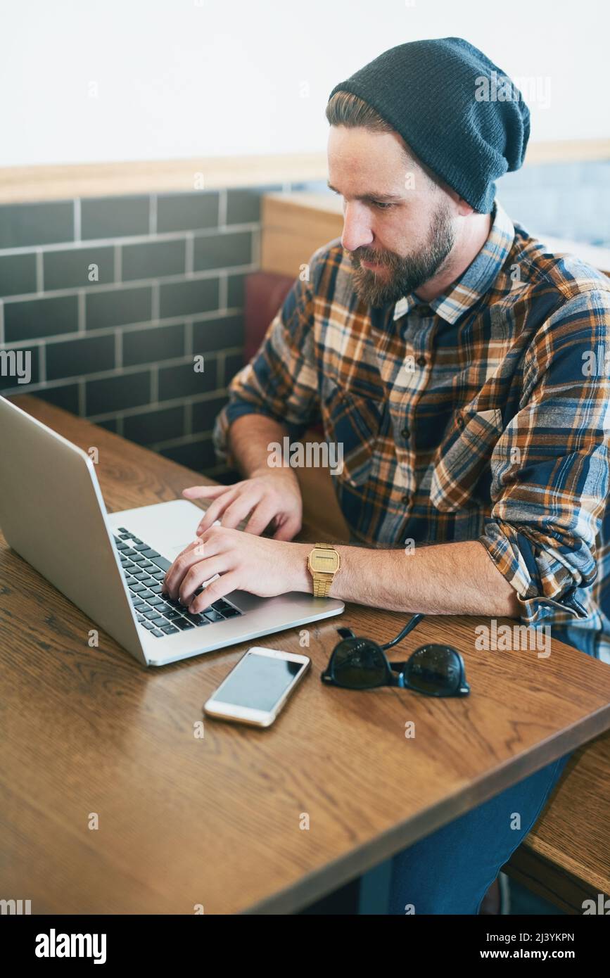 His office away from the office. Shot of a young man using his laptop while sitting in a cafe. Stock Photo