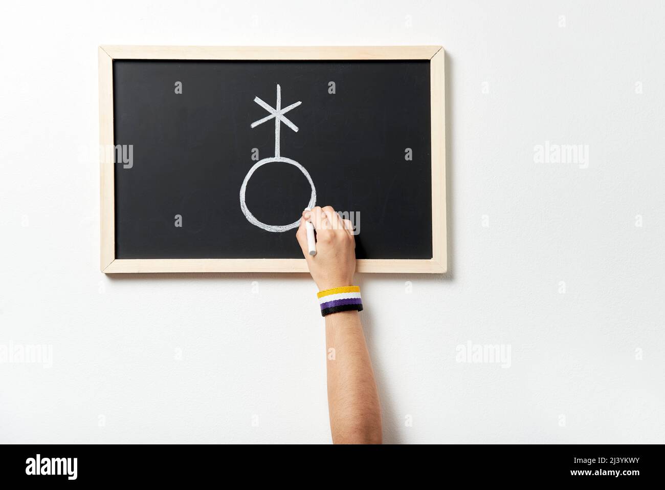 Hand with symbolic bracelet drawing on a chalkboard the symbol of the non-binary or genderqueer community Concept of respect for gender diversity. Stock Photo