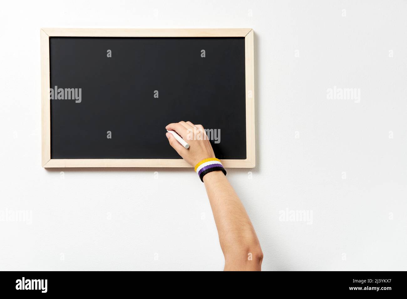 Hand with symbolic bracelet writing on a blank blackboard. Concept of respect for gender diversity. Stock Photo