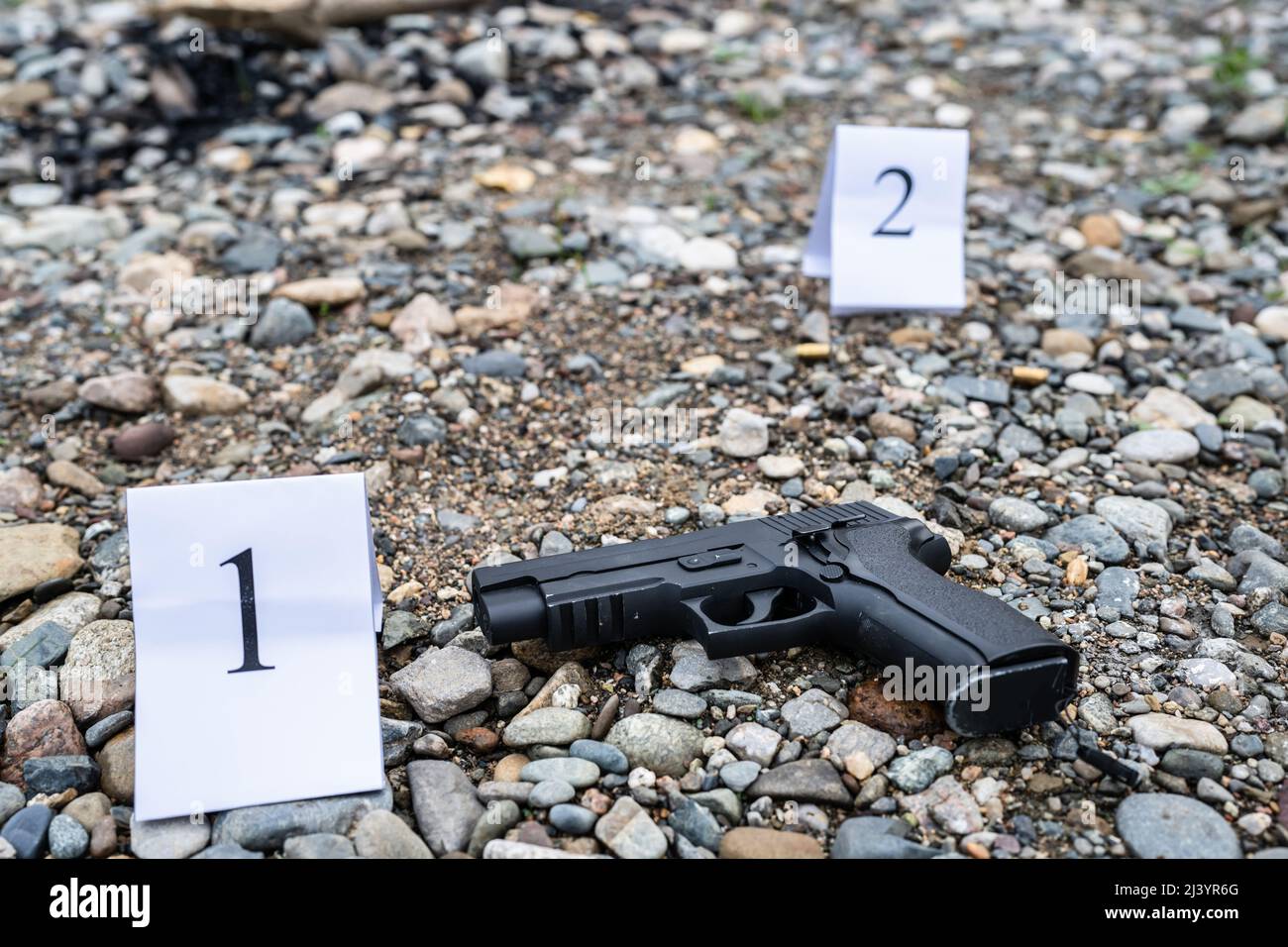 gun on the crime scene evidence on the beach or sand rocks used for murder or shooting with tag during investigation Stock Photo