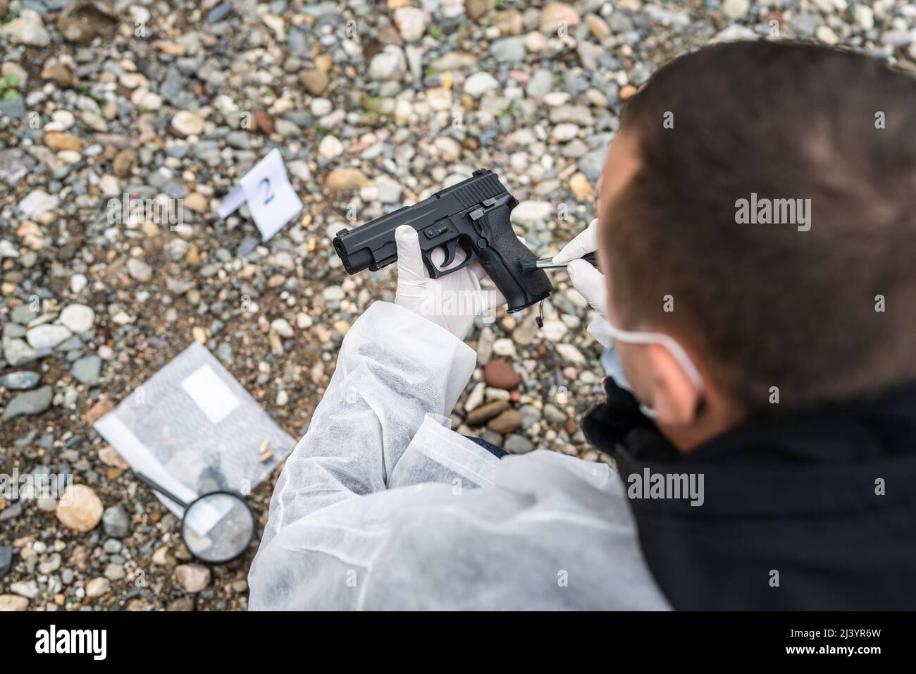 top view back of the police detective forensic investigator on the crime scene hold gun evidence on the beach or sand rocks used for murder or shootin Stock Photo