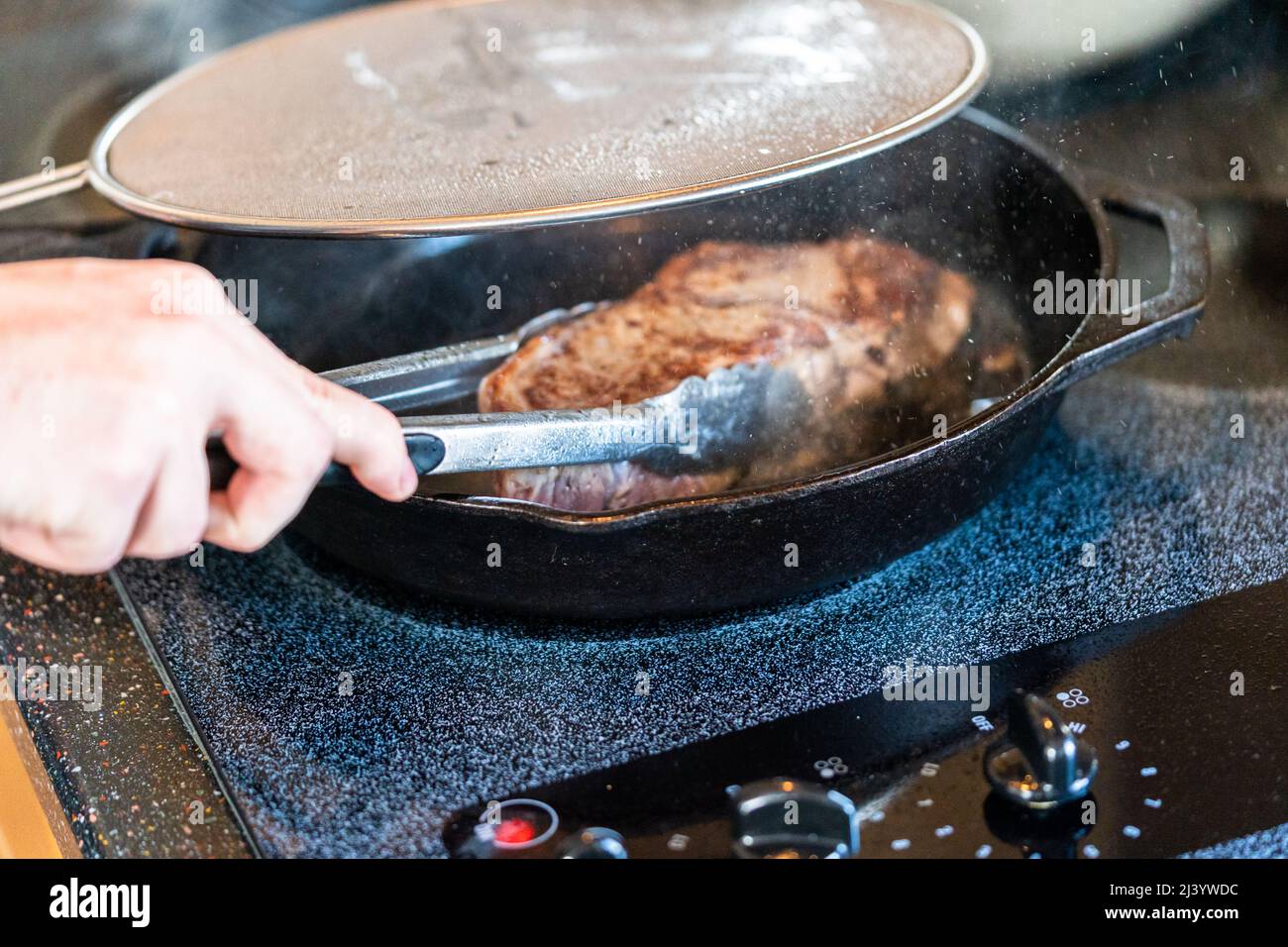 Frying New York strip steak in cast iron frying pan over the electric stove Stock Photo Alamy