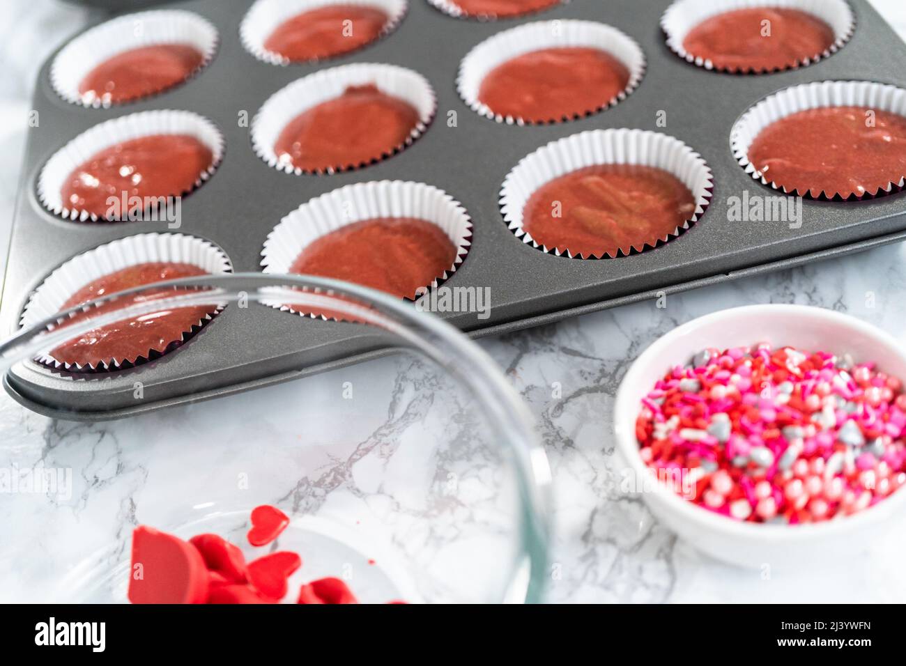 Scooping cupcake batter into a cupcake pan to bake red velvet cupcakes ...