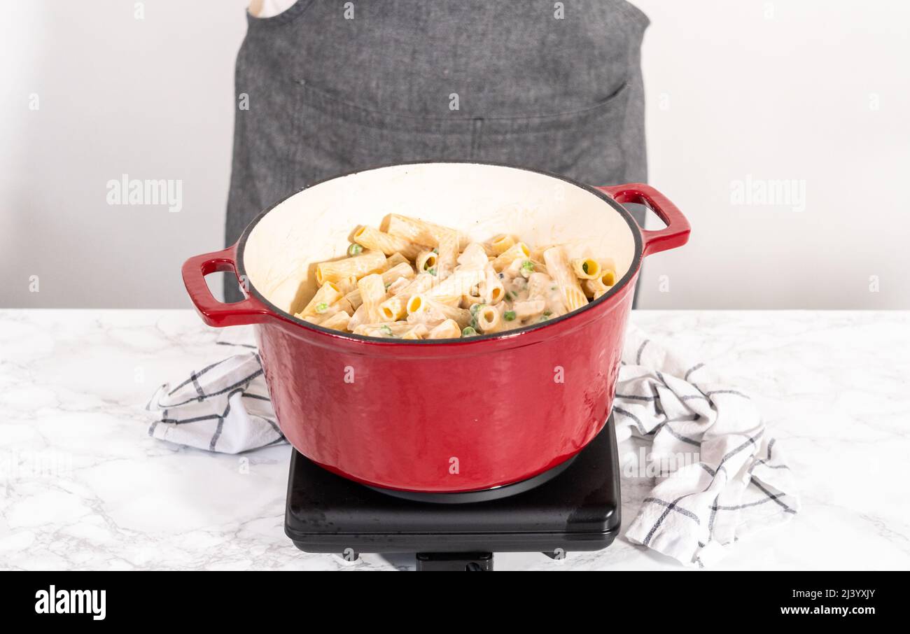 Mixing ingredients in an enameled dutch oven to prepare chicken alfredo pasta Stock Photo Alamy
