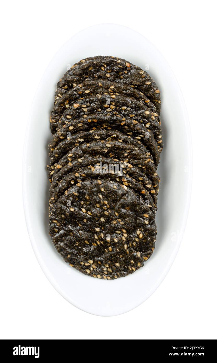 Sesame crackers, in a white bowl. Japanese senbei, crispy macrobiotic crackers, made of brown rice, black sesame seeds and soy sauce. Crunchy snack. Stock Photo