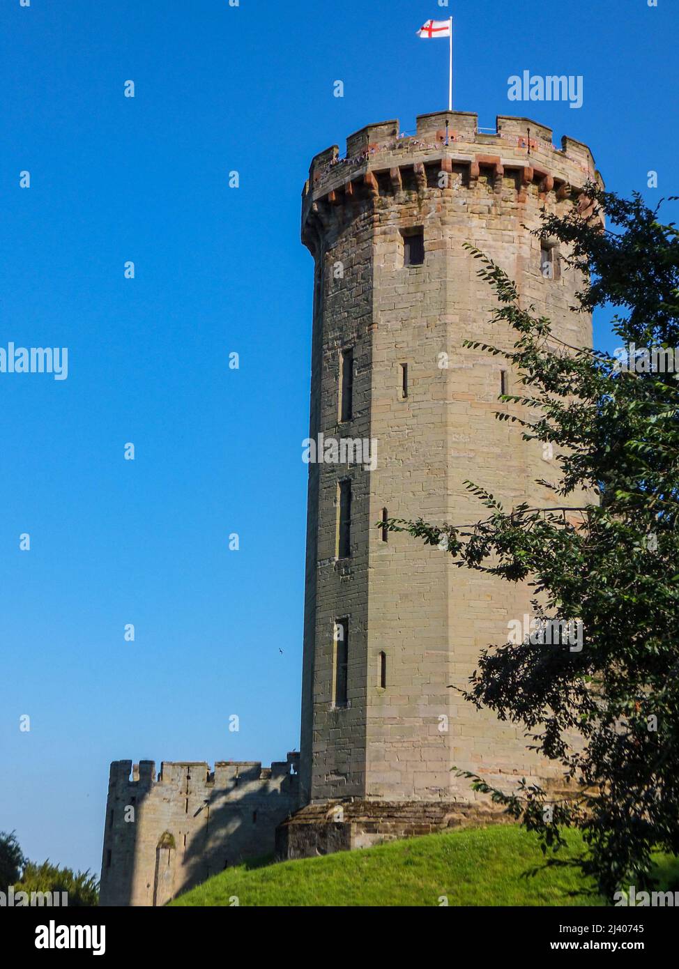 The English flag flies in the blue sky over the castellated Guy's Tower at medieval Warwick Castle in Warwickshire, England, UK. Stock Photo
