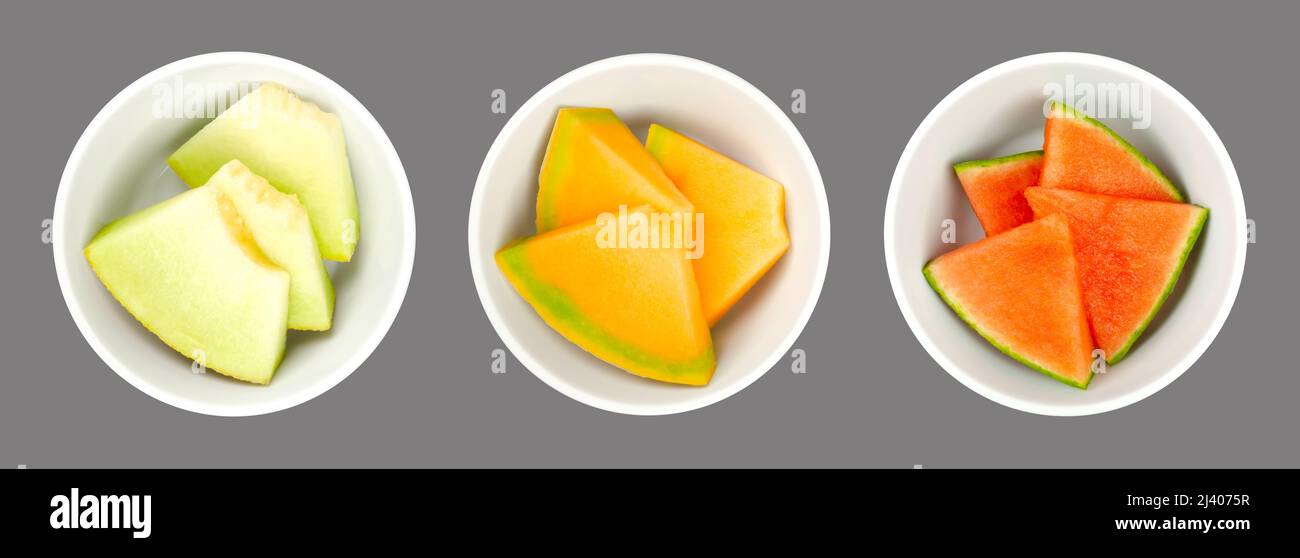Melon slices, in white bowls, over gray. Galia, honey Cantaloupe melon and watermelon. Freshly cut, triangular shaped pieces. Stock Photo