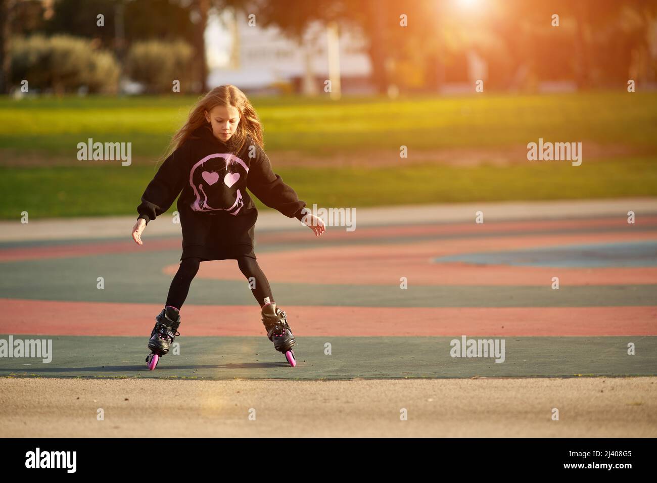 Little pretty happy funny girl on roller skates at a park, learning to roller skate outdoors Stock Photo
