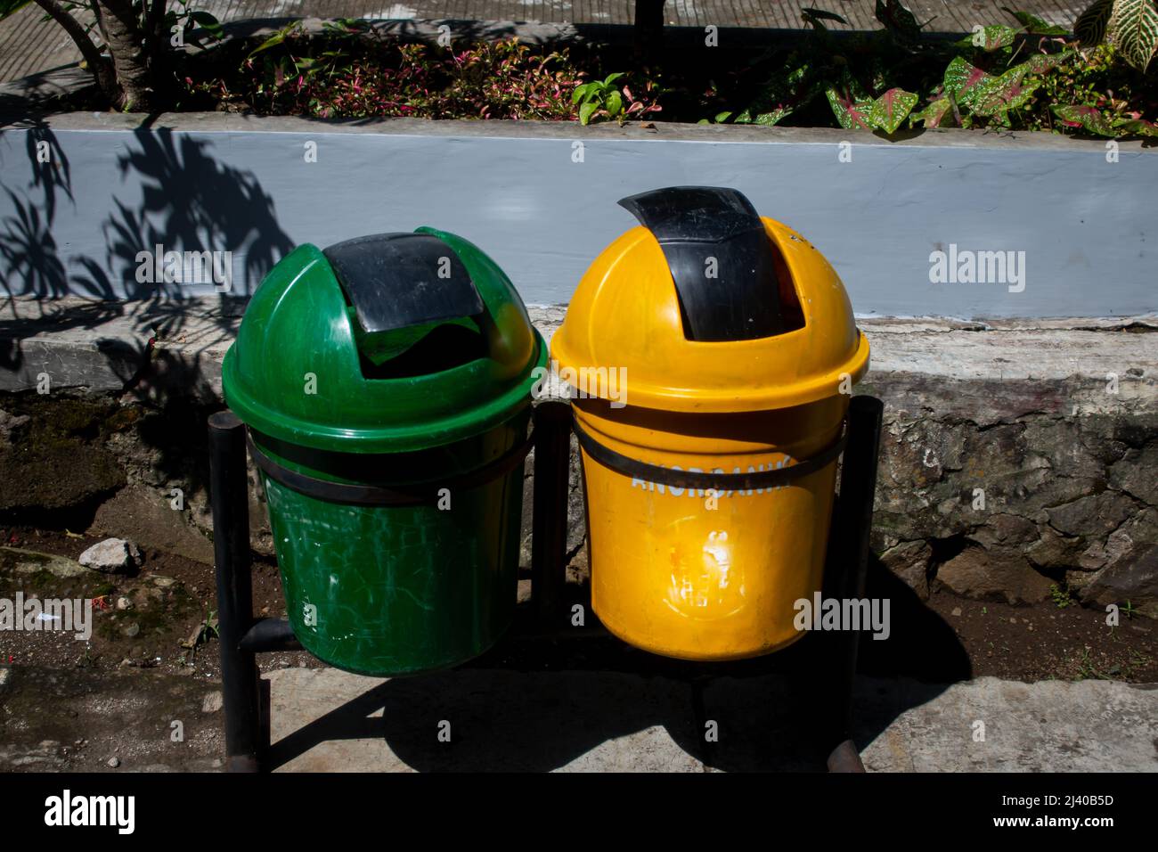 a pair of green and yellow trash cans, with black iron pillars, plant