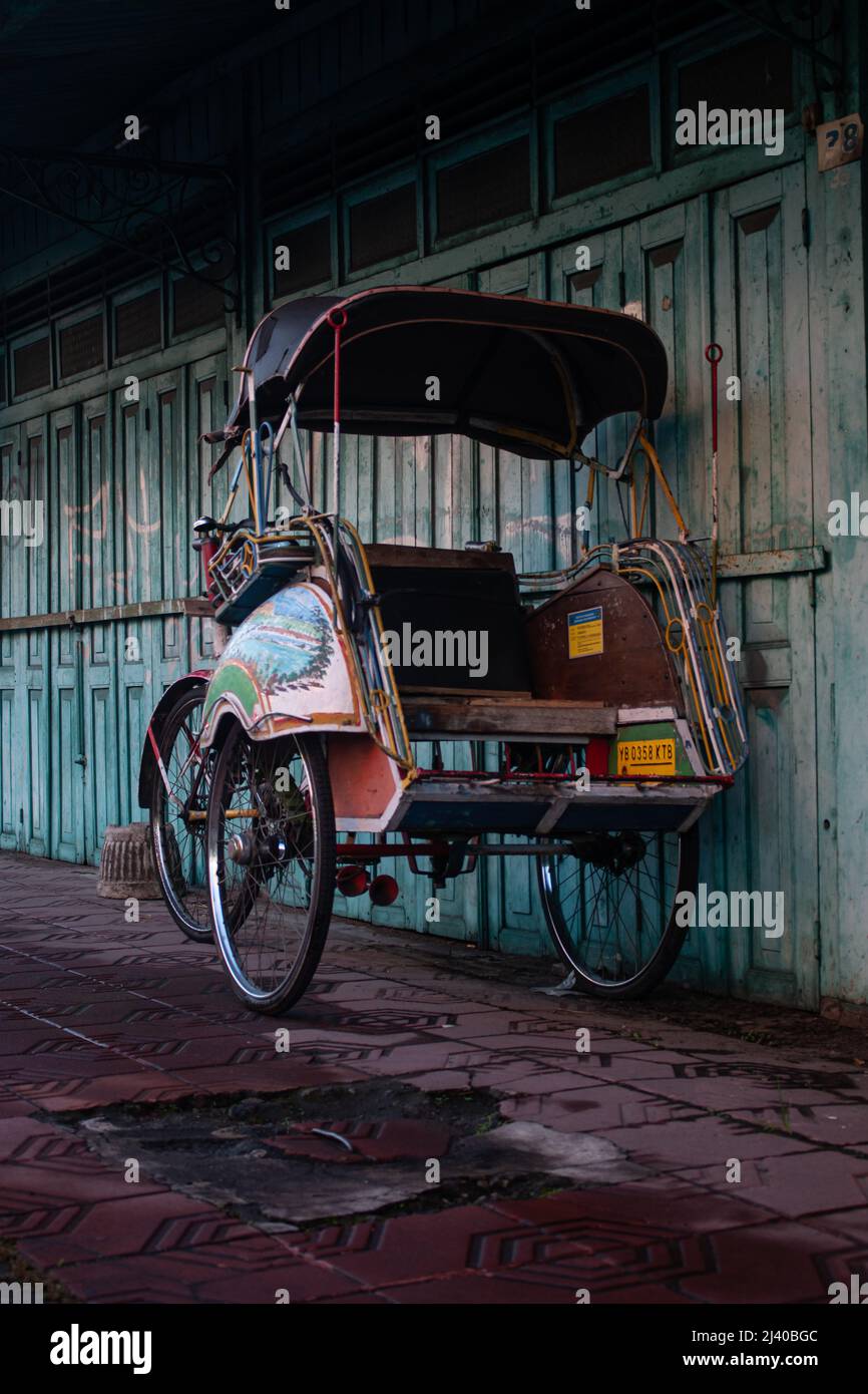 a classic rickshaw parked at a faded blue wooden door, red floors Stock Photo