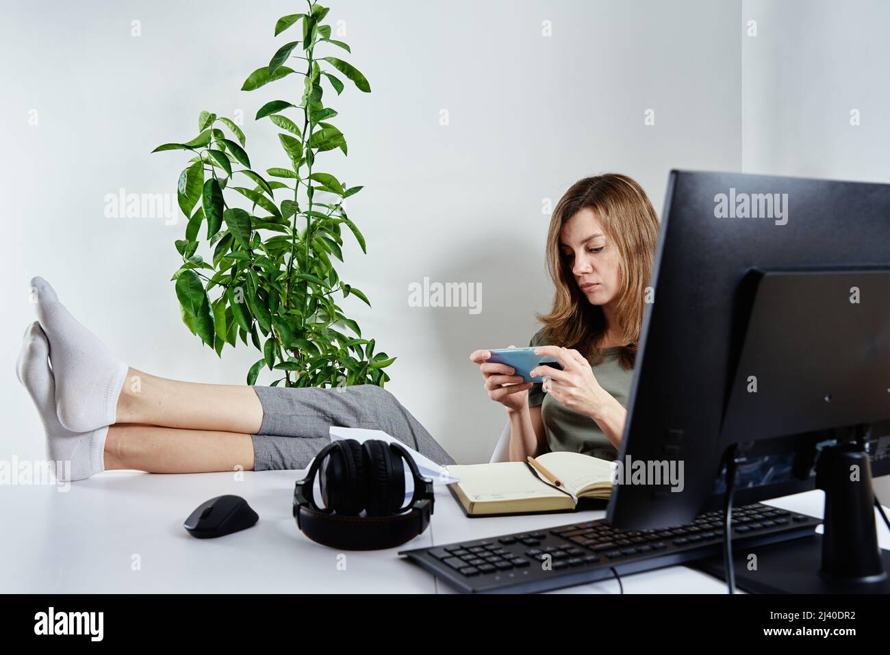 Woman procrastinate ar remote work. Freelancer use smartphone at home office. Unproductive office worker Stock Photo