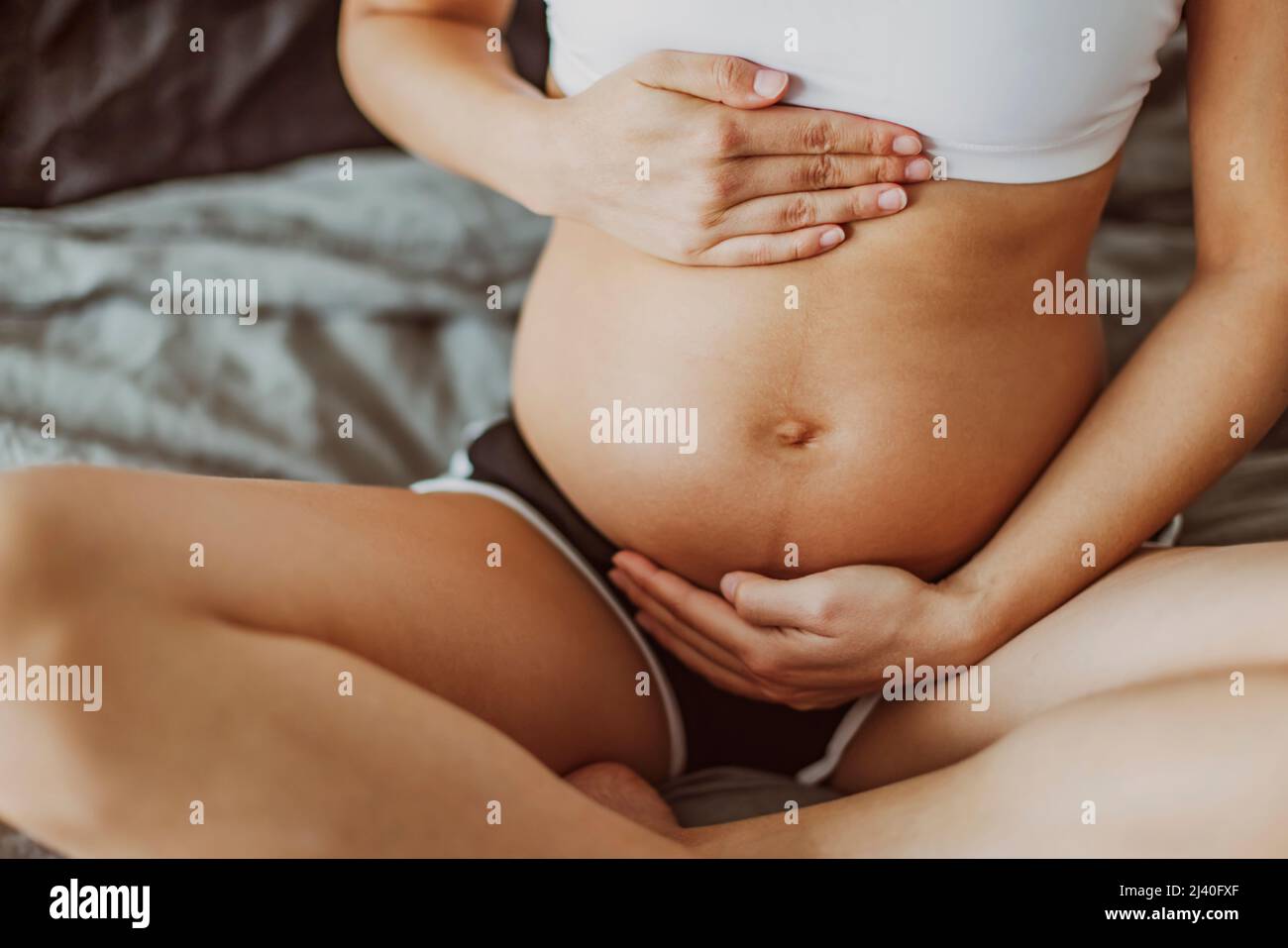 Pregnancy belly stretch marks and linea nigra. Pregnant woman caressing holding stomach during first trimester. Skincare body care health concept Stock Photo